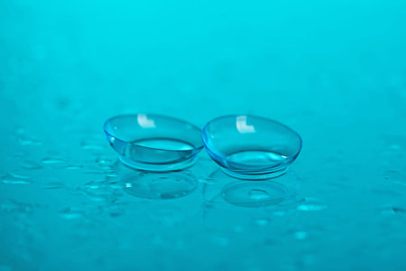 Pair of contact lenses and water drops on light blue mirror surface, closeupの写真素材