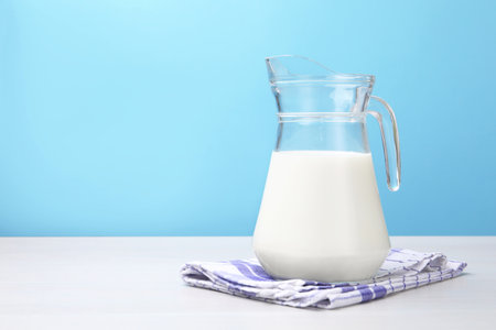 Fresh milk in jug on white wooden table against light blue background. Space for textの写真素材