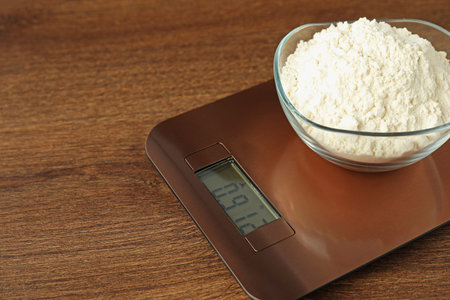 Modern electronic kitchen scale with bowl of flour on wooden table, closeup. Space for textの写真素材