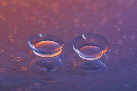 Pair of contact lenses and water drops on purple gradient mirror surface, closeupの写真素材