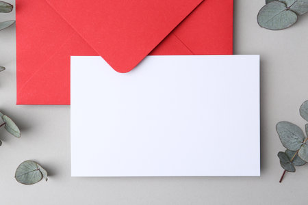Blank greeting card, paper envelope and eucalyptus leaves on light grey background, flat layの写真素材