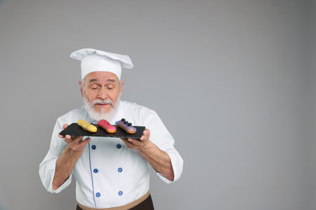 Professional pastry chef with delicious eclairs on grey backgroundの写真素材