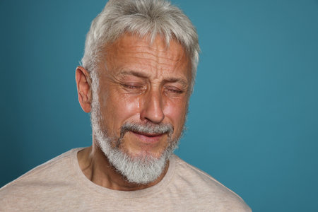 Sad man senior crying on light blue background, space for textの写真素材