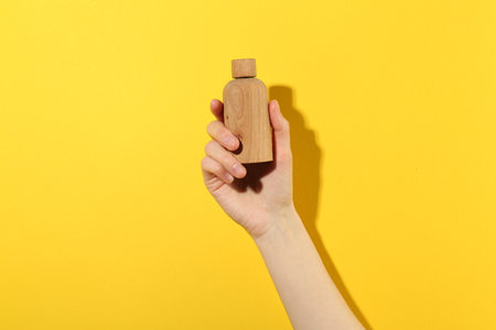Woman with bottle of serum on yellow background, closeup. Body care productの写真素材