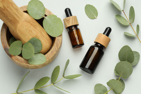 Bottles of essential oil, eucalyptus leaves, mortar and pestle on white background, flat layの写真素材