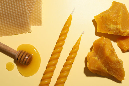 Beautiful beeswax candles, dipper with honey, pieces and sheets of wax on beige background, flat layの写真素材