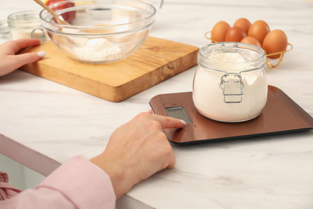 Woman weighing jar of flour on electronic kitchen scale indoors, closeupの写真素材