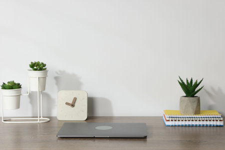 Laptop, stationery, floral decor and alarm clock on wooden office table against white backgroundの写真素材