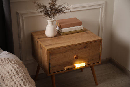 Glowing modern LED lamp on wooden bedside table indoorsの写真素材