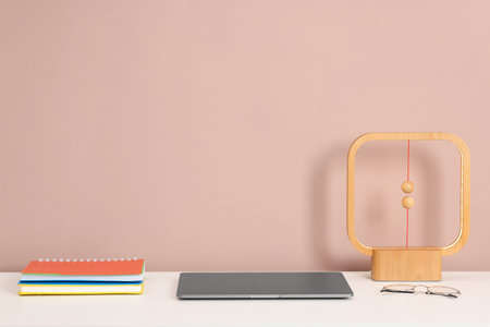 Laptop, stationery, lamp and glasses on white office table against dark beige background