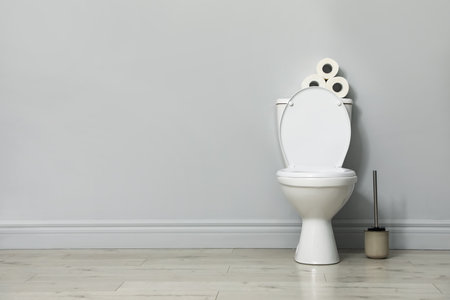 Ceramic toilet bowl, brush and paper near grey wall indoors. Space for textの写真素材