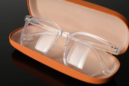 Stylish glasses in case on grey mirror surface, closeup