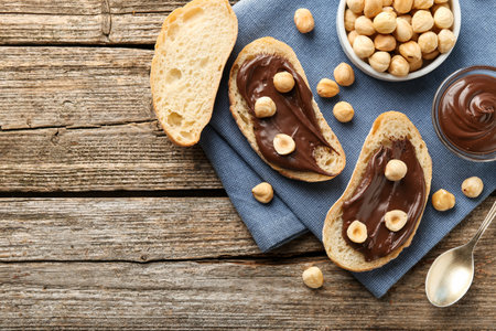 Slices of bread with chocolate spread and hazelnuts on wooden table, flat lay. Space for textの写真素材