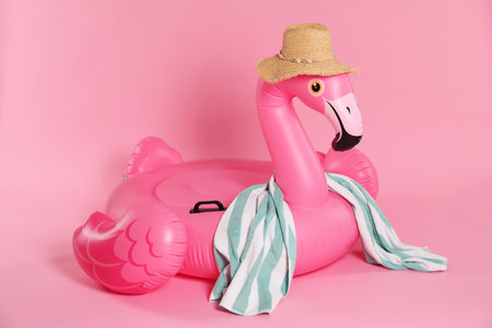 Inflatable flamingo shaped ring, straw hat and beach towel on pink backgroundの写真素材