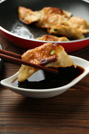 Dipping tasty fried gyoza (dumpling) into soy sauce on wooden table, closeupの写真素材