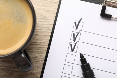 Checklist with marked checkboxes, marker and coffee on wooden table, flat layの写真素材
