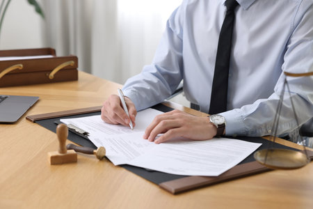 Notary signing document at wooden table in office, closeup