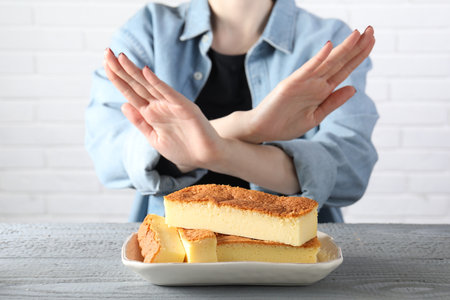 Woman refusing to eat cheesecake at grey wooden table, selective focus. Food allergy conceptの写真素材