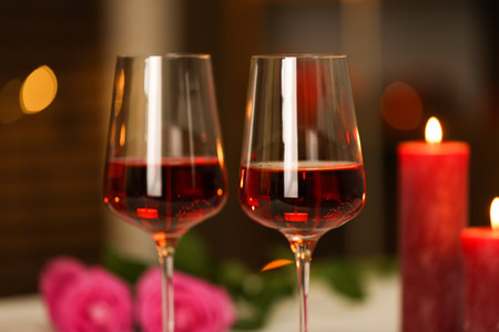 Glasses of red wine and burning candles against blurred background, closeup. Romantic dinnerの写真素材