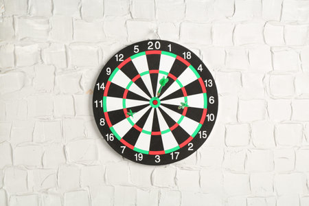 Dart board with arrows on white brick wall
