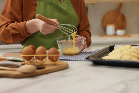 Woman whisking egg wash near raw croissants at white marble table in kitchen, closeupの写真素材