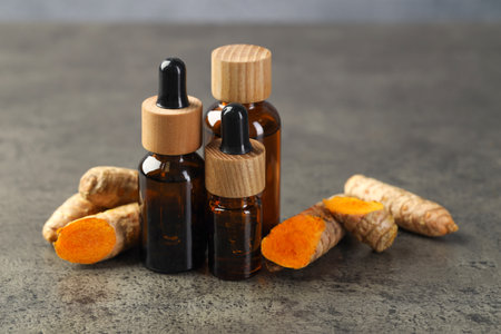 Tumeric oil and roots on grey table, closeupの写真素材