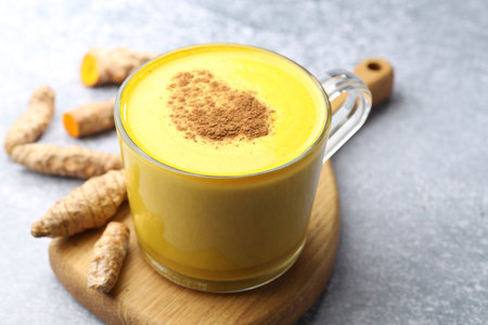 Tasty turmeric latte in cup and roots on gray table, closeupの写真素材