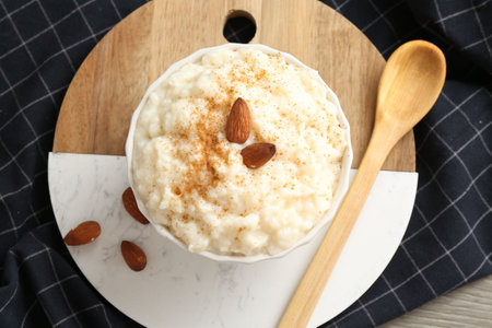 Delicious rice pudding with cinnamon, almonds and spoon on wooden table, top viewの写真素材