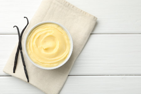 Tasty vanilla pudding and pods on white wooden table, top view. Space for textの写真素材