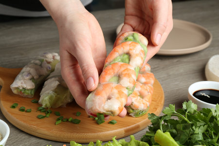 Woman making tasty spring roll at gray wooden table, closeupの写真素材