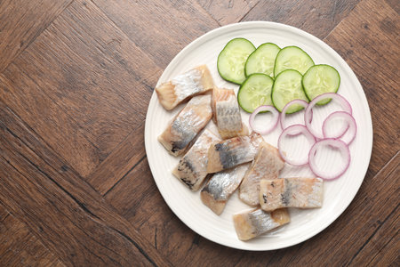Pieces of delicious herring, onions and cucumber slices on wooden table, top view. Space for textの写真素材