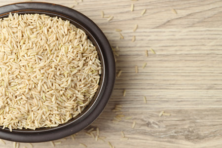 Brown rice in bowl on wooden table, top view. Space for textの写真素材