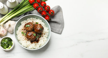 Delicious rice with meatballs, sauce and green onions on white marble table, flat lay. Space for textの写真素材