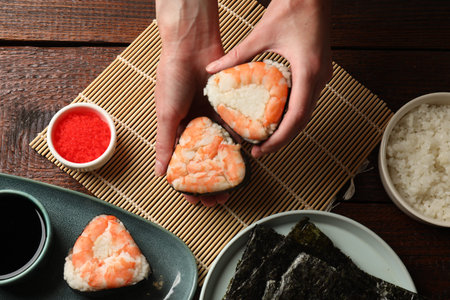 Woman holding tasty onigiri (Japanese rice balls) with shrimps at wooden table, top view