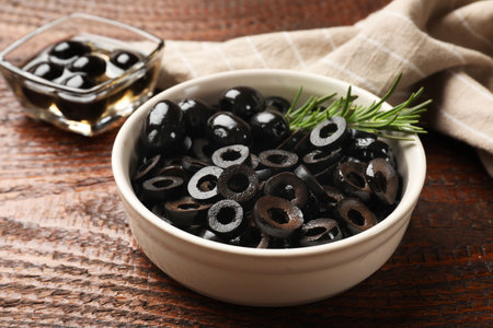 Delicious marinated olive rings and rosemary in bowl on wooden table, closeupの写真素材