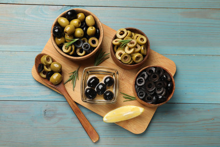 Different delicious marinated olive rings, whole ones and rosemary on light blue wooden table, flat layの写真素材
