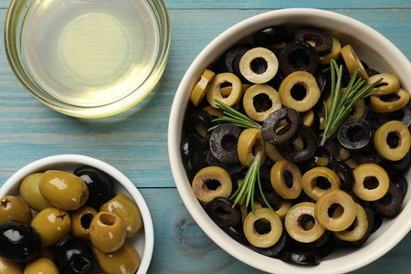 Different delicious marinated olive rings, whole ones, rosemary and oil on light blue wooden table, flat layの写真素材