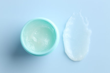 Moisturizing lip balm and jar on light blue background, top view