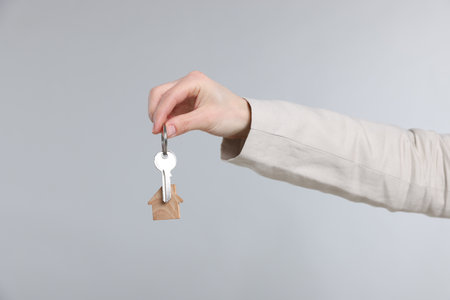 Real estate agent holding key with house shaped keychain on gray background, closeupの写真素材