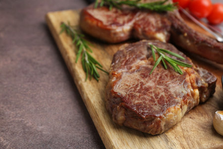 Pieces of delicious beef meat with rosemary on brown table, closeup. Space for textの写真素材