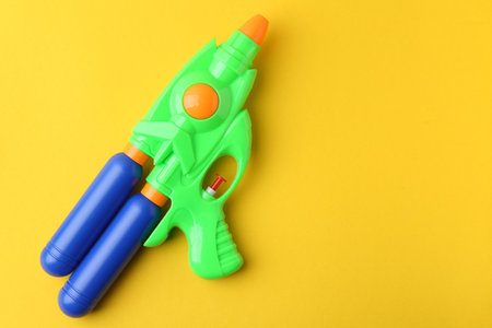 Bright plastic water gun on yellow background, top view. Space for textの写真素材