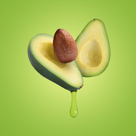 Halves of avocado with dripping oil in air on bright backgroundの写真素材