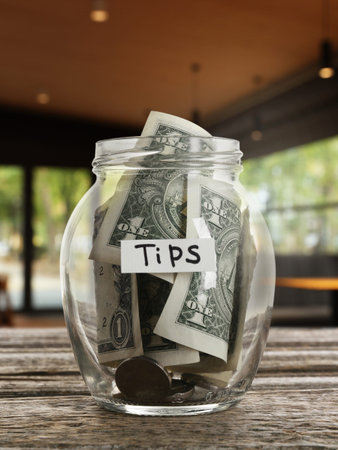 Tips jar with money on wooden table in cafe