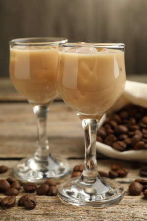Coffee cream liqueur in glasses and beans on wooden table, closeup