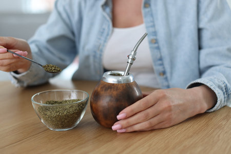 Woman making traditional yerba mate tea at wooden table indoors, closeup