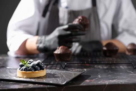 Confectioner with chocolate muffin at dark table, focus on tart