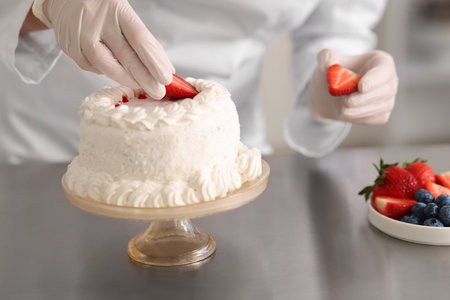 Confectioner decorating cake with strawberries at table, closeupの写真素材