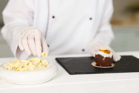 Confectioner decorating tasty dessert at white wooden table in kitchen, closeupの写真素材