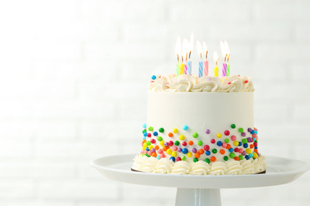 Delicious cake with colorful sprinkles and burning candles against blurred white background, closeup. Space for textの写真素材