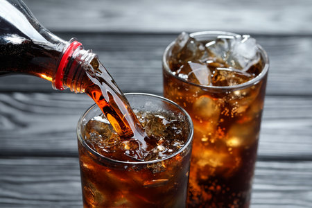 Pouring refreshing cola from bottle into glass at grey wooden table, closeupの写真素材